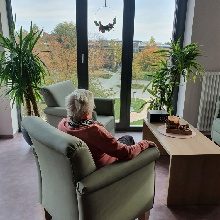 Eine Bewohnerin sitzt gemütlich im Sessel und blickt aus dem Fenster auf die Parkanlage | Copyright: Diakonieverein Burghof e. V.
