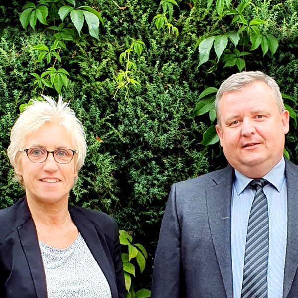 Abbildung des Vorstands: Frau Lazay und Herr Umnus stehen im Außenbereich vor einer Hecke