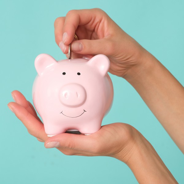 Kleines Sparschwein auf einer Hand und ein Geldstück wird reingesteckt